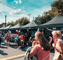 Two young women in the foreground walking through a line of tent booths on a blue-skyed sunny day