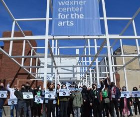 Workers holding signs under the Wexner Center for the Arts sign on building