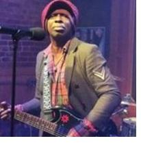 Black man in a hat playing a guitar at a mic
