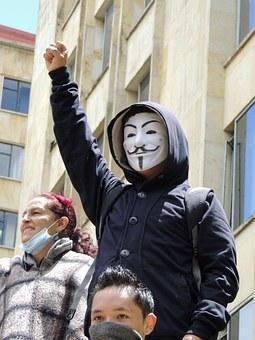 Guy wearing anonymous Guy Fawkes mask with fist in air at protest with others 