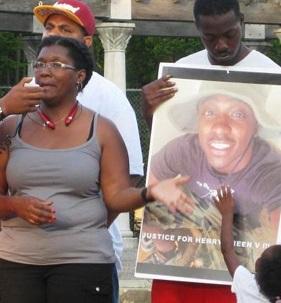 Black woman talking and pointing to photo of her son, young black man