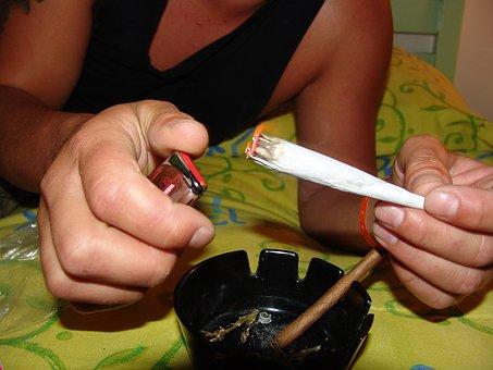 Person's hands lighting a huge joint over an ashtray