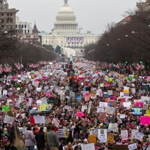 Building with round white  dome, tree lined street, lots of protestors wearing pink