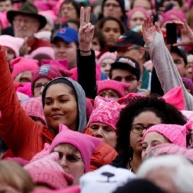 Lots of young women of different races wearing pink in a huge crowd with peace signs with their fingers in the air