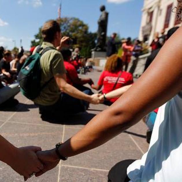People sitting on ground holding hands and women in foreground holding someone's hand