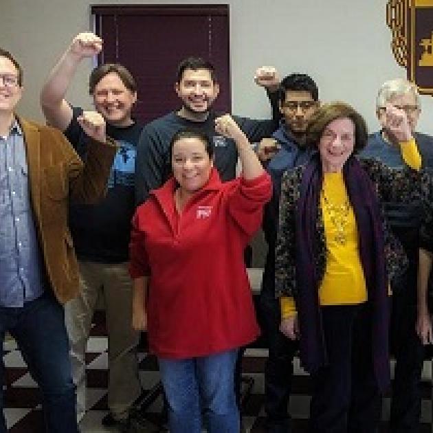 Several people smiling and standing in rows facing the camera with their fists in the air