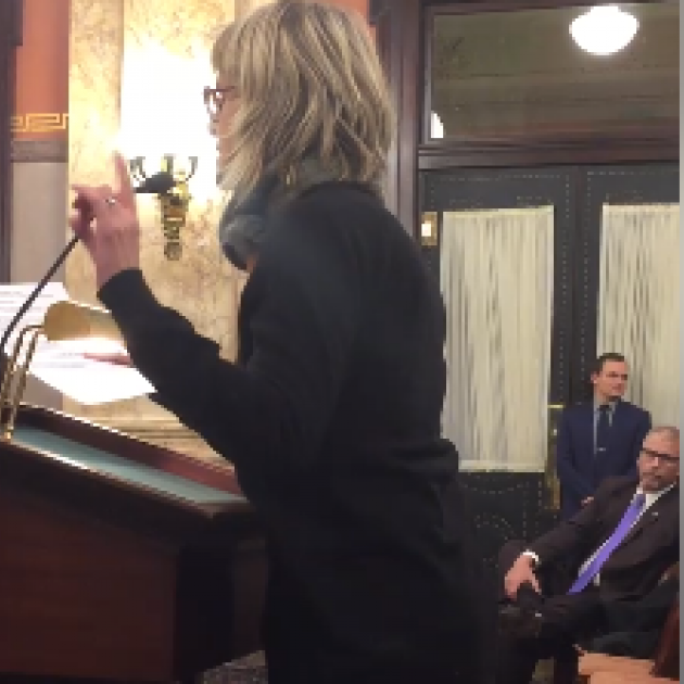 White woman with short blonde hair taking animatedly at a podium