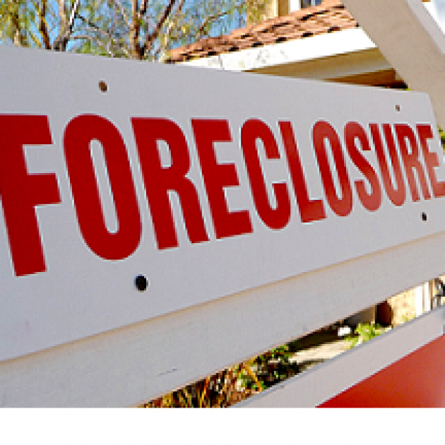 White sign with red letters saying Forclosure in front of a house