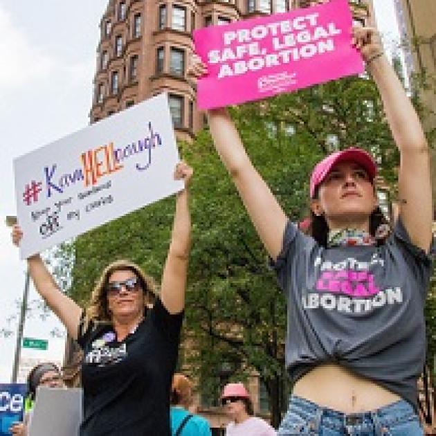 Two white women holding pro-choice signs above their heads looking very determined outside at a rally