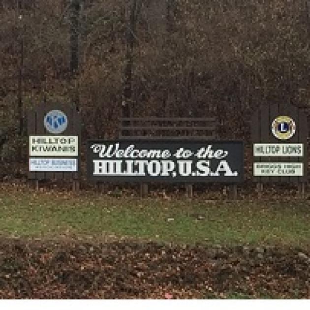 Long outdoor sign in front of trees saying Welcome to the Hilltop USA
