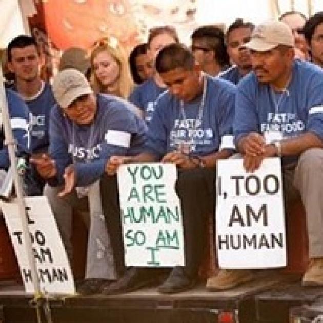 Latino men wearing blue shirts sitting and holding signs that say I Too, Am Human