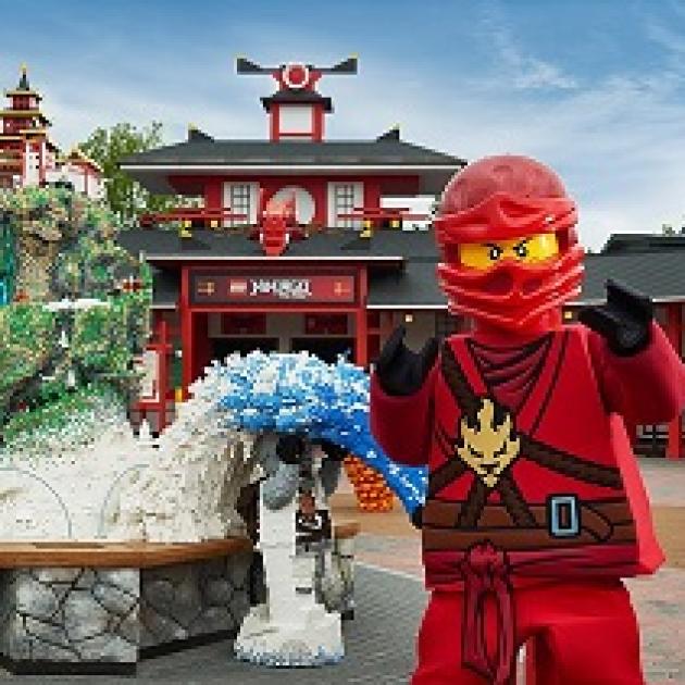Robot looking character in red suit and helmet standing by and in front of structures made out of legos