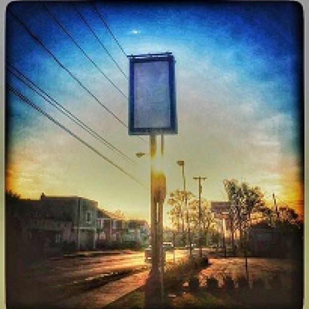 Blue background sky with a tall rectangular sign that is blank on a city street