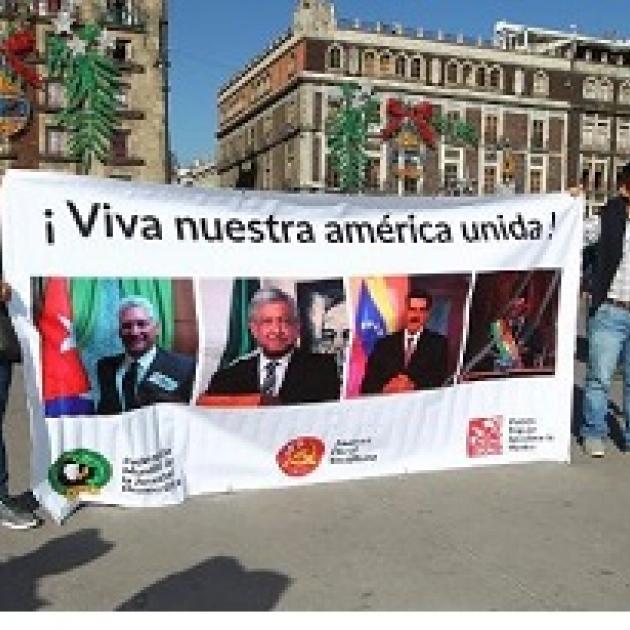 People holding a big banner outside that says Viva nuestra america unida! and a lot of faces of people