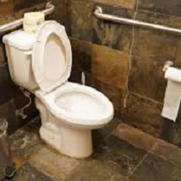 White toilet with lid up and toilet paper roll on hanger on wall under a silver bar against a brown tile wall and floor