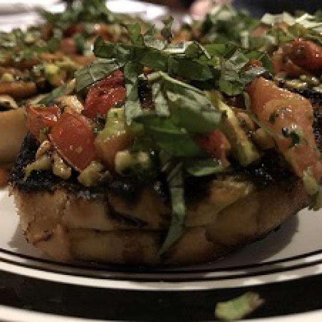 A piece of food on a plate with other similar items, looks like a baked potato with lots of greens, tomatoes, other brownish things on top.