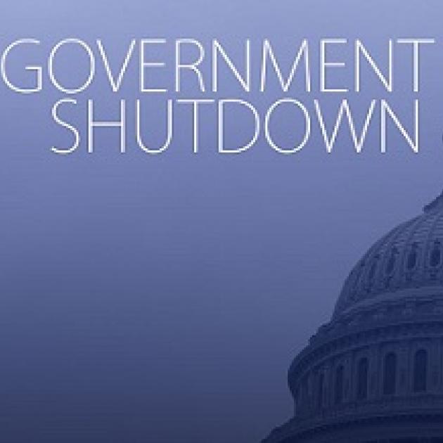 Blue background white letters saying Government Shutdown and the edge of the capitol building in DC