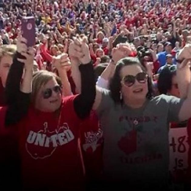 Lots of people in the background and in the foreground two heavyset middle aged ladies holding hands with arms above their heads in victory pose