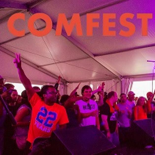 Purplish and reddish hues in a photo of several young people, black and white, holding their fingers as peace signs in the air, cheering and clapping under a tent with the words COMFEST in orange at top