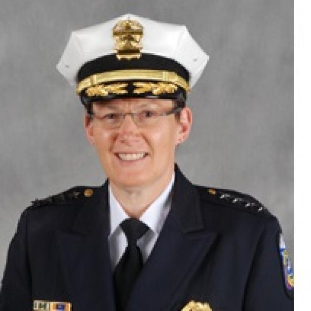 White woman in a police uniform and wire rimmed glasses smiling and posing
