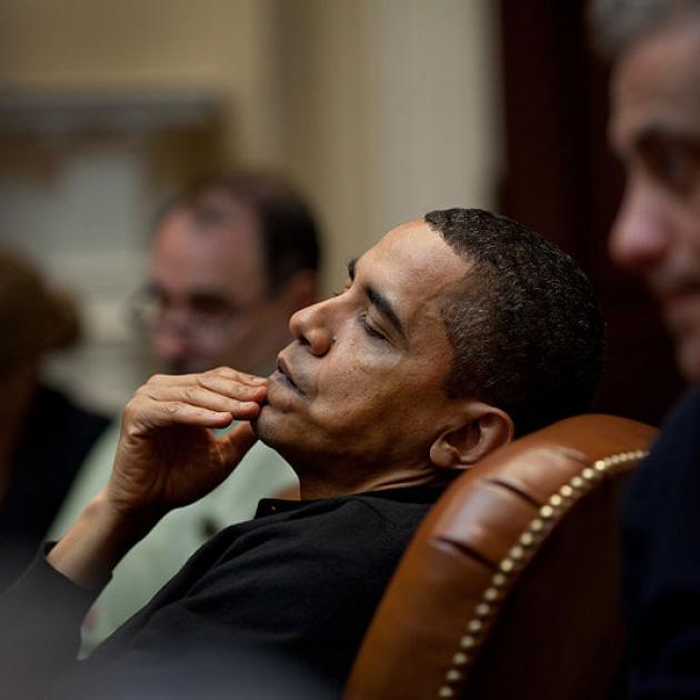 Obama leaning back in leather chair with hand on mouth looking pensive