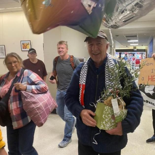 Man walking through airport holding a plant with people and balloons surrounding him