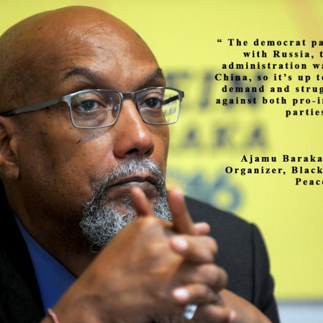 Bald black man with hands folded in front of chin, wearing glasses and with a gray goatee against yellow background and some words