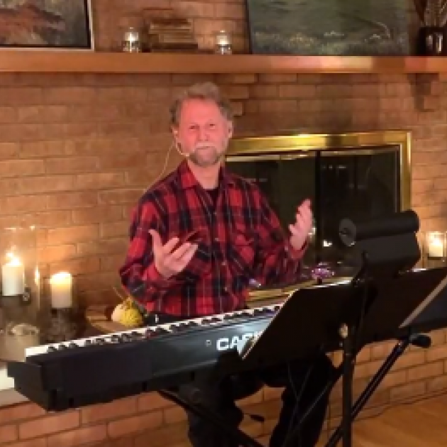 White man at a keyboard in front of a fireplace