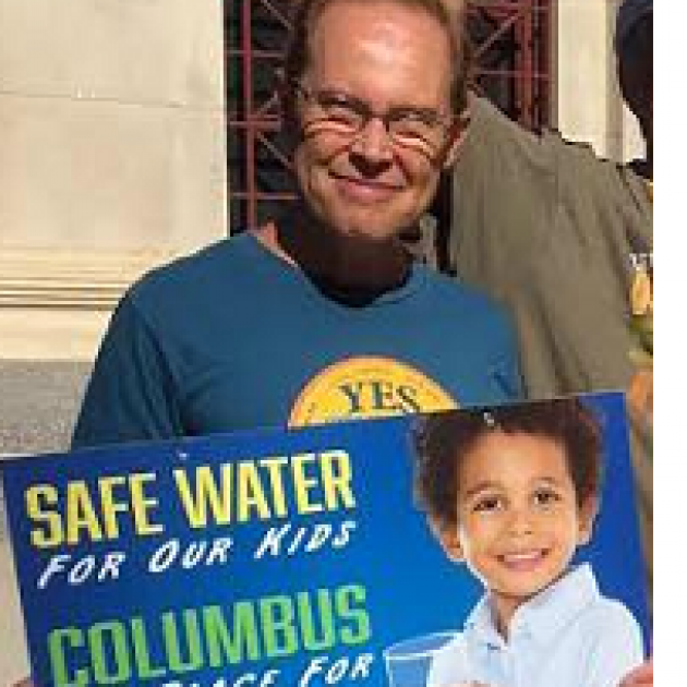 White man smiling and holding a sign saying Safe Water for our Kids
