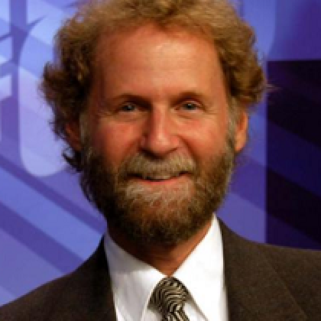 Photo of man with light brown curly hair and moustache and beard smiling in a suit