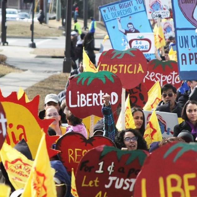 People holding bright red signs shaped like tomatoes that say Justica and Libertad