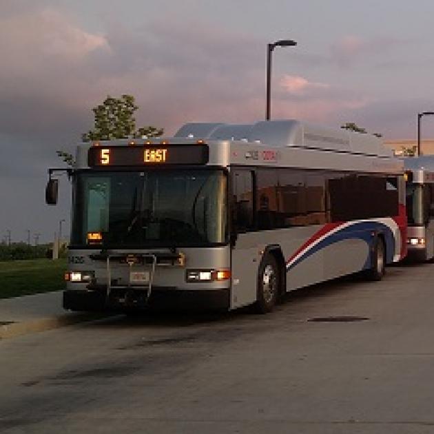 COTA bus, sllver bus with red white and blue curvy stripe on side driving in dusk