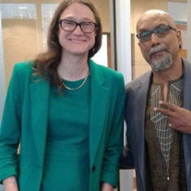Tall thin white woman smiling with glasses and a green dress next to an older black man in a suit making a peace sign