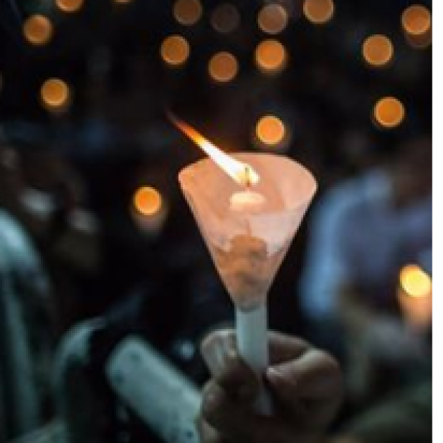 Night time scene close up of a hand holding a candle glowing in the dark with other glowing candles in the background