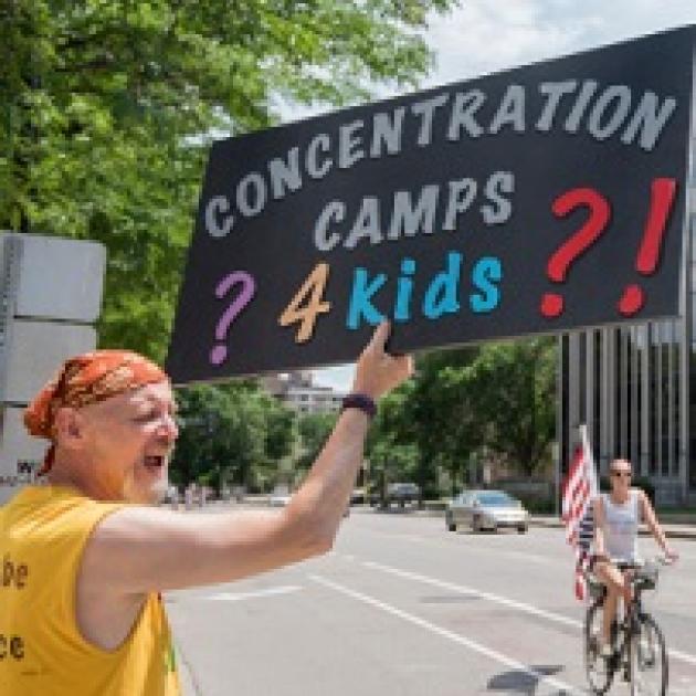 White man in a bandanna and yellow shirt yelling and holding a sign that reads Concentration Camps 4 Kids with lots of question marks