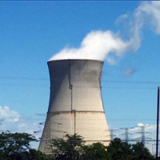 Big fat nuclear plant smokestack with white smoke billowing out against a blue sky