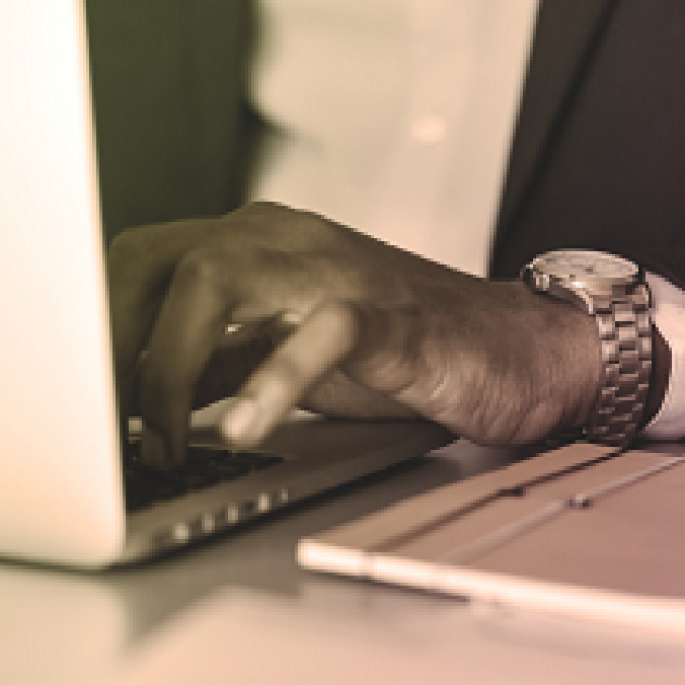 Extreme close up of black man's hand wearing a watch typing on a laptop