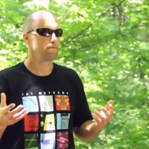 Young white man mostly bald holding his hands out in front of him standing in a forest