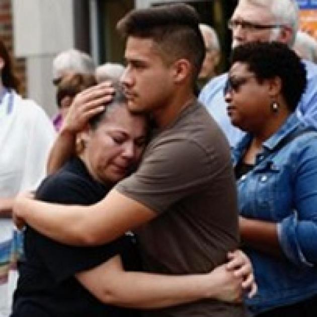 Young man hugging a shorter older woman with other people looking on in the background