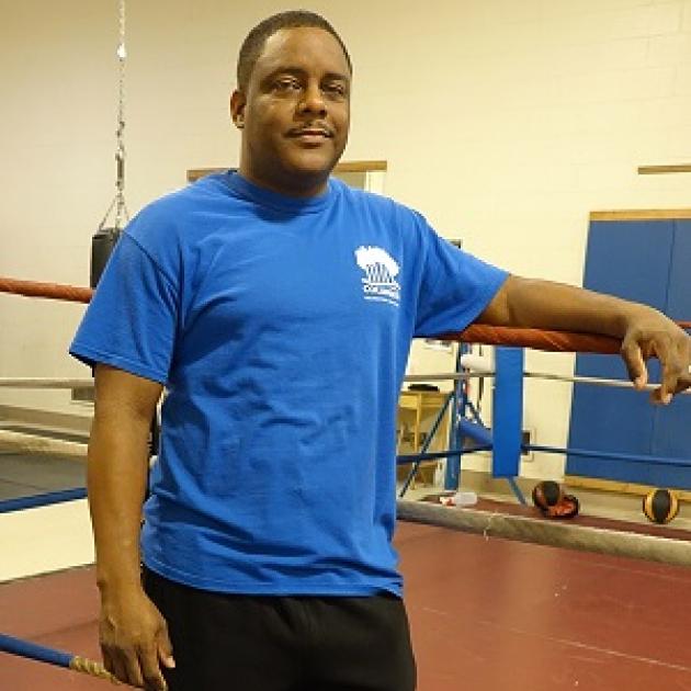 Black man in blue t-shirt standing next to a boxing ring