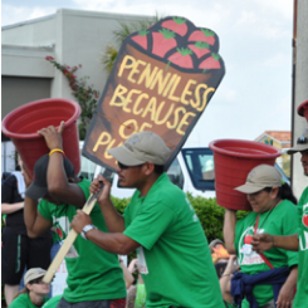 People of color in green shirts marching and holding signs one that says Penniless 