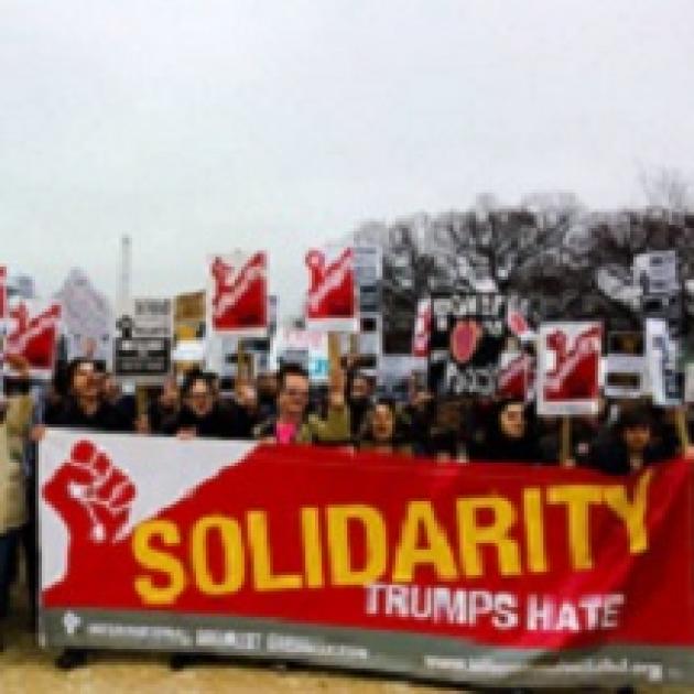 Lots of people at a march front ones holding a long red and white banner saying Solidarity Trumps Hate with a fist 