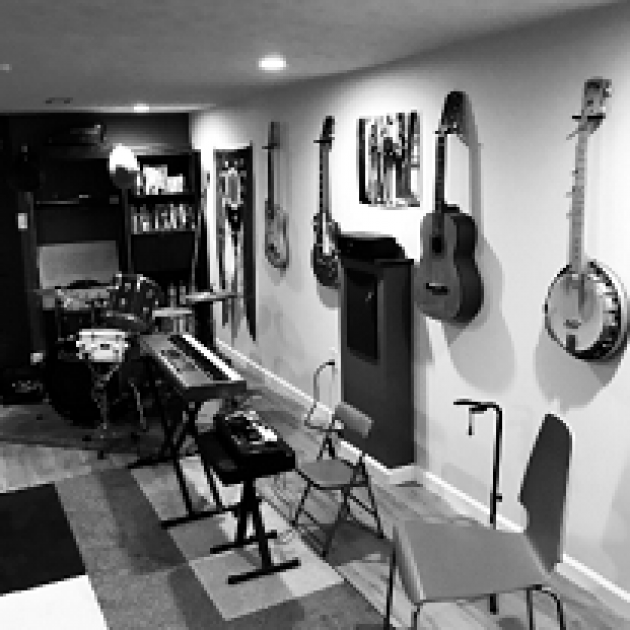 Black and white photo of room with lots of guitars and a banjo hanging on the wall and other musical instruments