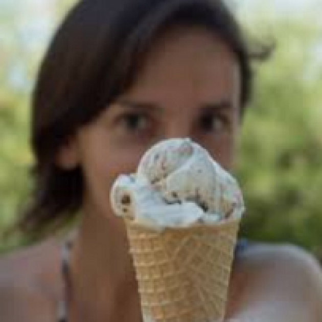 Young white girl with brown hair holding an ice cream cone in front of her face