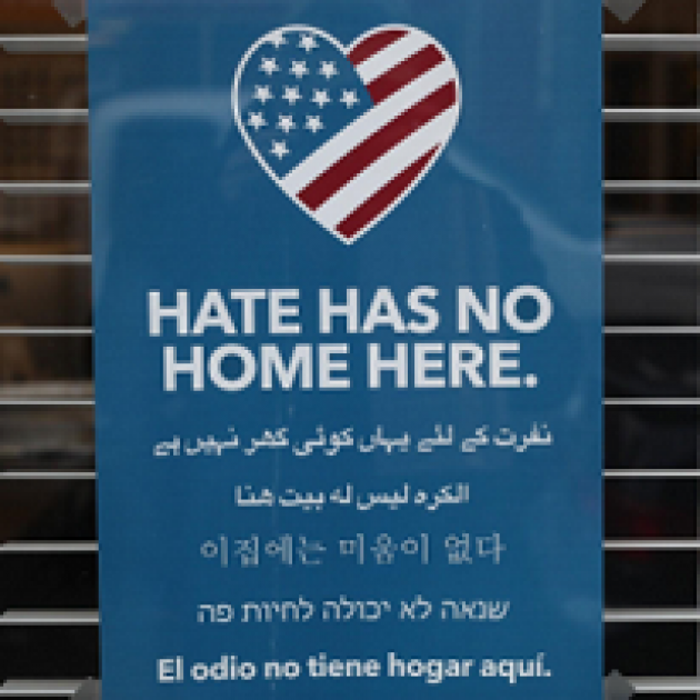 Blue sign with a heart that has a flag and words Hate has no home here