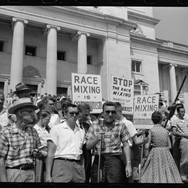 Black and white photo of protest in streets from 50s with sign saying something about race mixing
