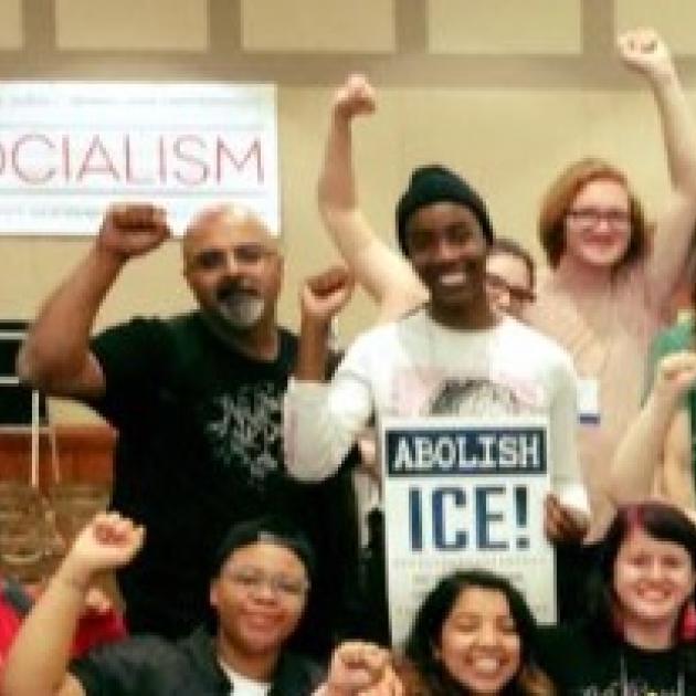 People smiling with fists in the air and a sign that says Socialism and one that says Abolish ICE