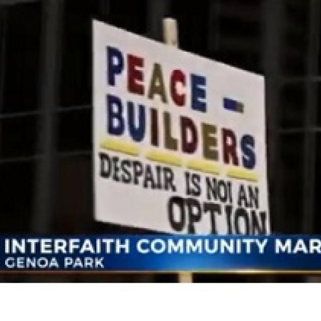 Words on a picket sign Peace Builders Despair is not an option and the banner lower third below saying Interfaith Community March, Genoa Park