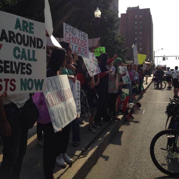 View down a sidewalk with people holding signs demonstrating and some bike cops facing them