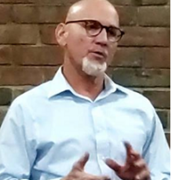 Bald white man with glasses with white goatee talking and making hand gestures